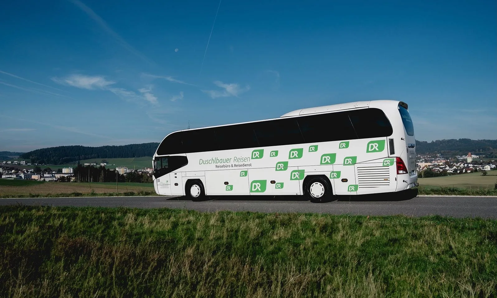 Reisebus von Duschlbauer Reisen auf einer Landstraße unter blauem Himmel