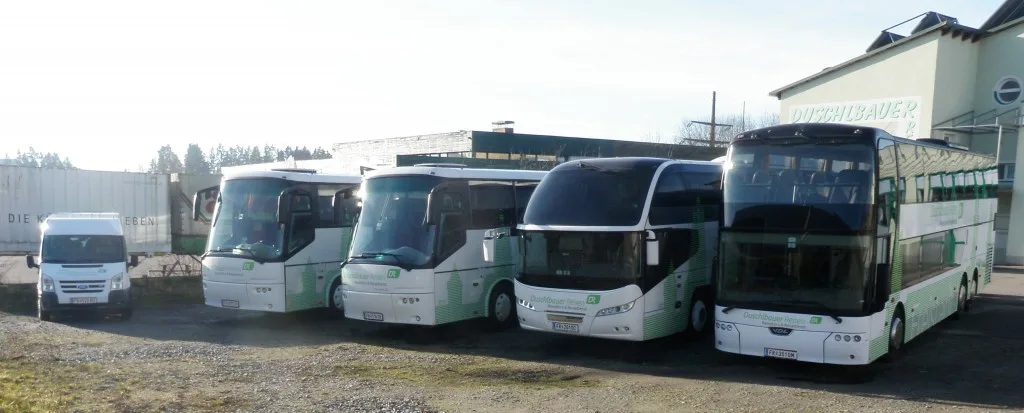 Mehrere Reisebusse von Duschlbauer nebeneinander vor dem Gebäude mit Schriftzug Duschlbauer, rechts ein Doppeldecker