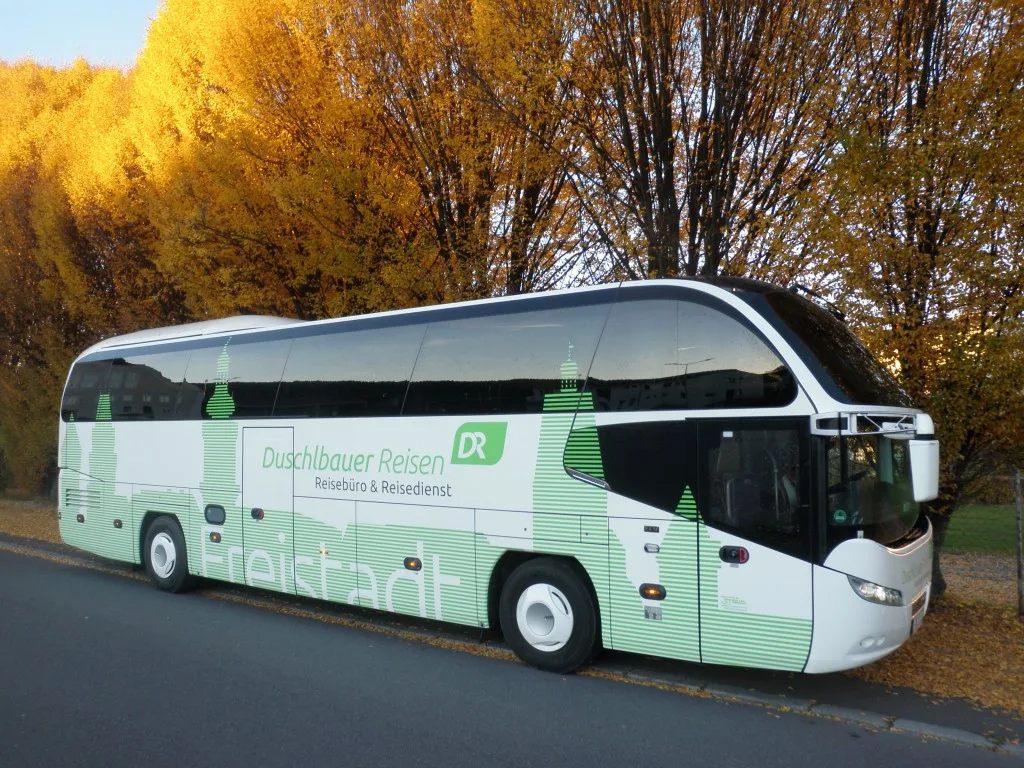 Neoplan-Reisebus von Duschlbauer Reisen mit großem Schriftzug Freistadt auf der Seitenwand, dahinter Bäume mit Herbstlaub